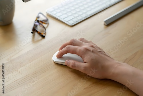 Hand holding a mouse on a desk, with a computer keyboard