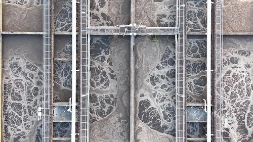 Aerial view of a water purification system showing sedimentation tanks with swirling water and foam, highlighting the continuous flow of water treatment processes in an industrial setting
