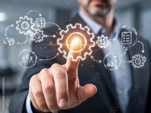 Business Process Optimization: A businessman's hand interacts with a digital interface, showcasing a network of gears and icons representing business processes and analytics.