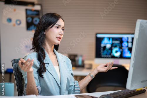 Young Asian Businesswoman Gesturing While Working with AI Technology on Computer in Modern Office