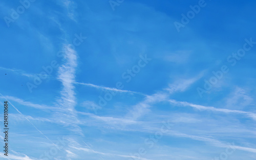 Foto Thin white contrails from airplanes crisscross a clear bright blue sky with scattered wispy cirrus clouds and two distant small birds flying high above