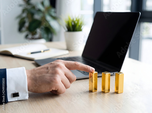 Businessman hand pushing golden blocks on a desk with a laptop