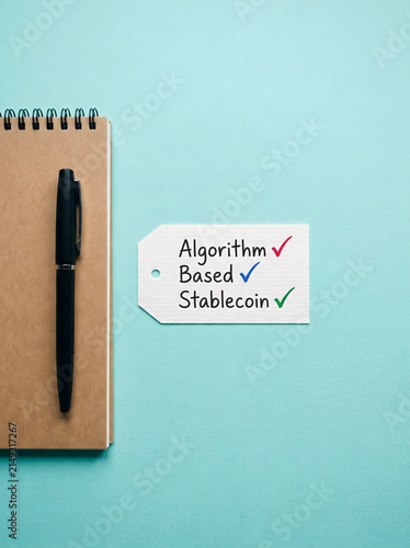 Algorithm based stablecoin text on a paper tag next to a notebook with a pen on a green surface