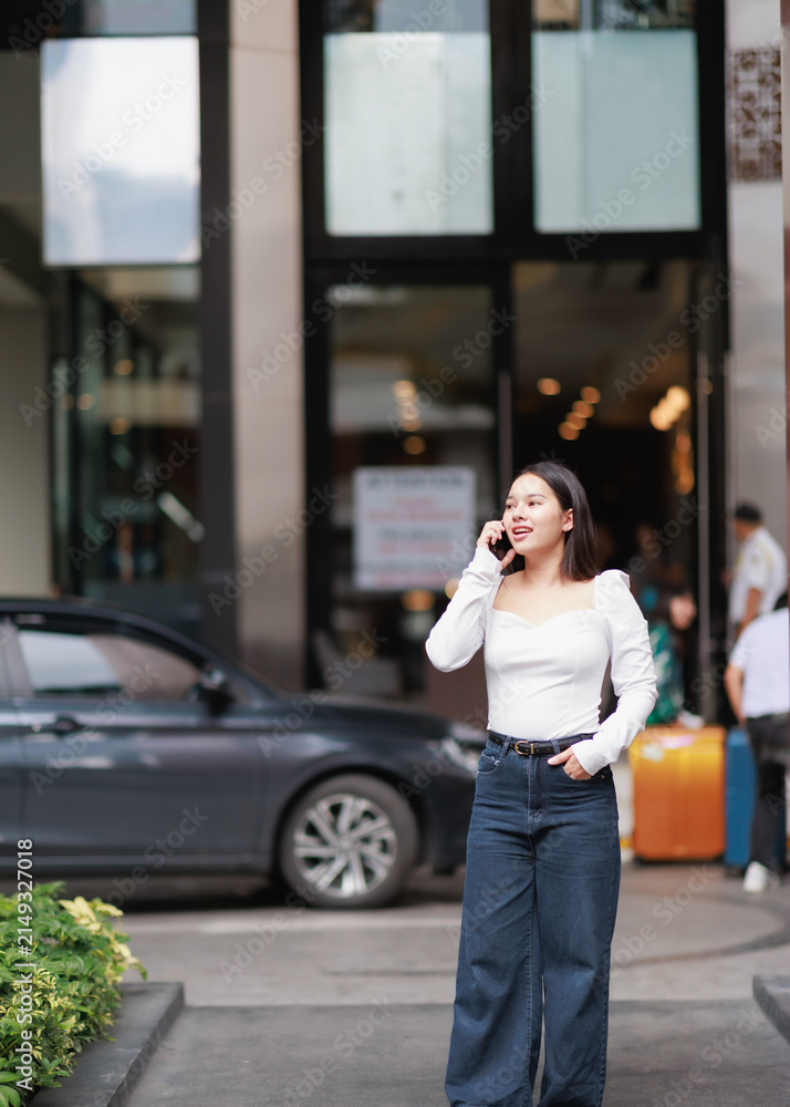 Fototapeta premium Young woman having a conversation on a mobile phone, communicating with technology in an urban environment while standing on a city street