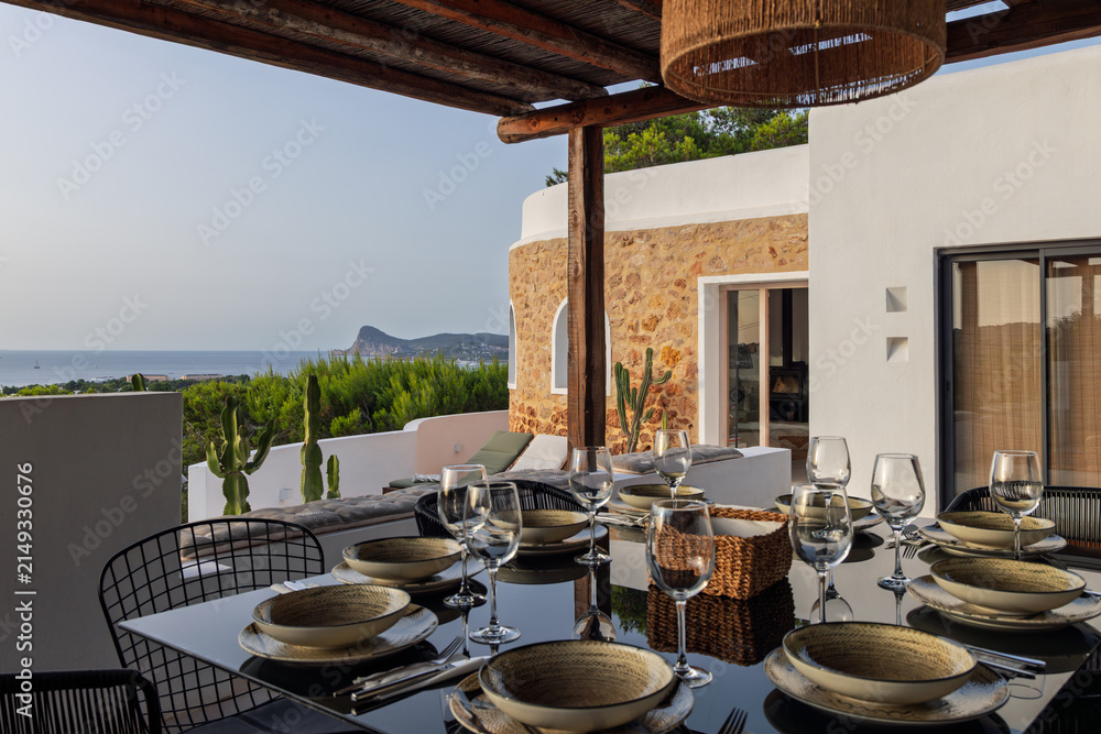 Fototapeta premium Villa dining terrace remains visible on Ibiza, Spain amid set dining table, photographed outdoors under warm late afternoon daylight.