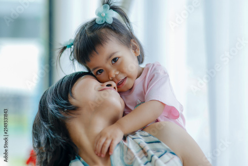 Happy mother carrying her little daughter on her shoulders, sharing joyful smiles that express love, family bonding, warmth, care, trust, and precious moments at home, Asian Thai people