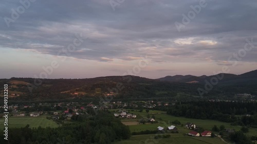 Drone view of countryside at evening time. Nature inspiration. Calming peace. Rural area with small buildings on background mountains landscape. Destination for tourism and wanderlust
