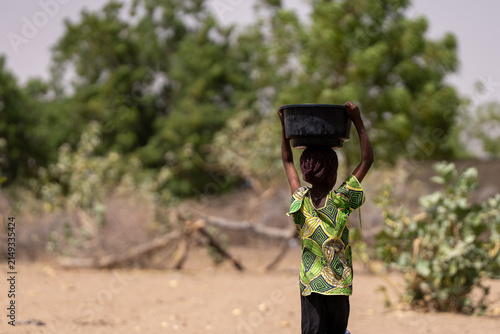 Foto Young girl carries heavy pot on head through dry landscape