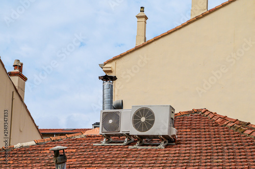 Two outdoor air conditioning units installed on a terracotta tiled roof