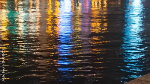 Colorful city light reflections on dark rippling water surface.