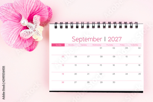 Desk calendar for September 2027 with pink orchid. Flat lay.