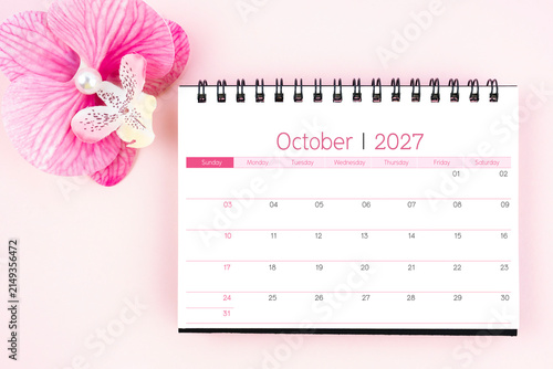 Desk calendar for October 2027 with pink orchid. Flat lay.