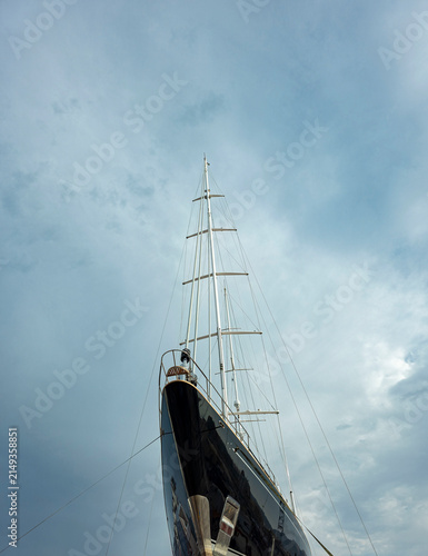 Canvas Print View of a black yacht bow and mast from below against a cloudy sky at a marina d