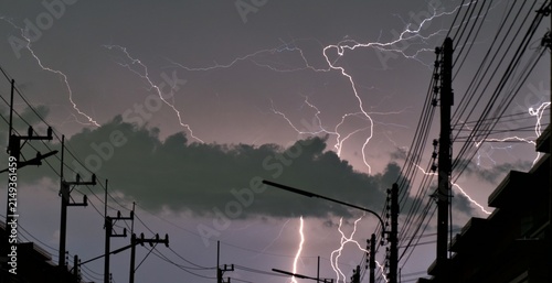 Fotografía Widespread lightning storm over an urban street with power lines and utility poles silhouetted against a dramatic cloudy night sky