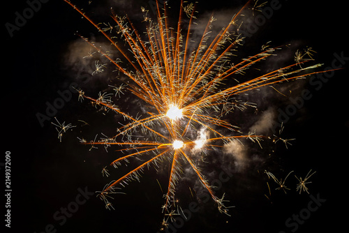 Golden fireworks display with radial orange rays and starbursts in the night sky.