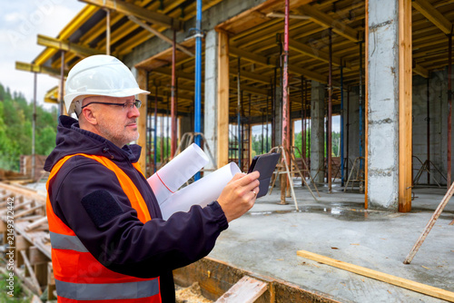 Construction Supervision. Site engineer checks building formwork and concrete structure using tablet and blueprints during construction quality inspection.