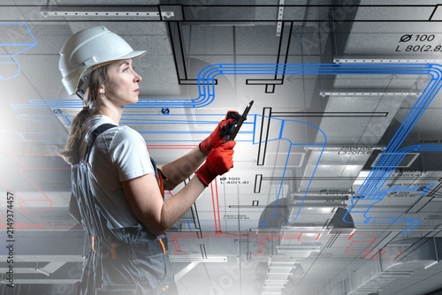 Engineering design: female engineer reviews building plans and HVAC systems using tablet with technical blueprint overlay.