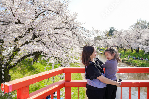View of embracing Mother and Daughter sightseeing at Cherry Blossom River View from Red Bridge sight seeing Sakura festival in Saita , Shinkawa River Japan