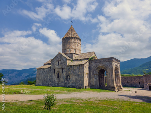 Historic Armenian Tatev monastery stands on grassy hillside near mountains