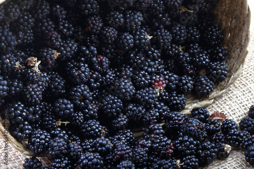 Close-up of fresh ripe blackberries spilling out of a woven basket onto a rustic burlap cloth