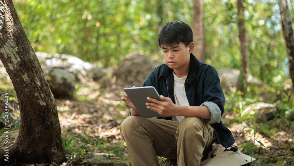 Fototapeta premium Asian Male Tourist Using Digital Tablet Sitting Forest Concept
