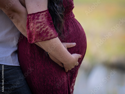 Close-up of an expectant couple embracing and gently holding a pregnant belly outdoors, symbolizing love, support and anticipation.