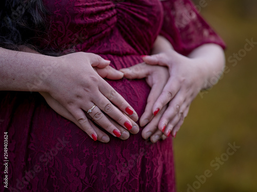 Close-up of two people gently holding a pregnant belly, symbolizing pregnancy, parenthood, love and anticipation.
