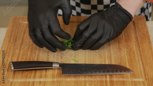 Chef finely chops fresh herbs on a wooden cutting board