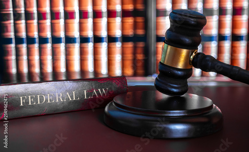 Federal Law book with wooden judge gavel on sound block in front of blurred law library bookshelf, court justice and legal system concept