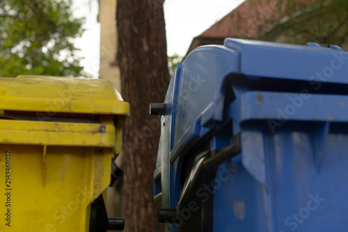Fotografie Streetlevel blue and yellow bins awaiting pickup on curb, shallow depth creating