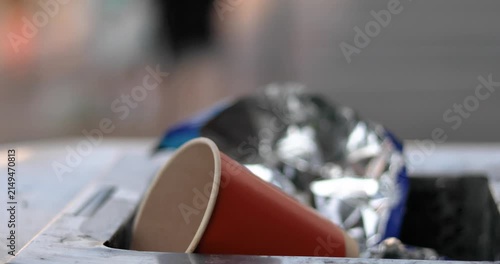A disposable used cup thrown into a trash bin in a public place near a roadway.