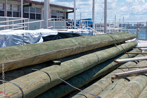 Obraz na płótnie Stacked treated wooden utility poles stored on a sunny waterfront dock near a ma