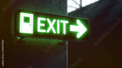 Green glowing rectangular light sign indicating emergency exit mounted on grey textured concrete wall in dark industrial corridor environment cinematic footage.