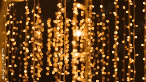 Strings of golden led fairy lights hanging vertically against dark background create warm festive ambiance with bokeh effect and soft cinematic camera motion.