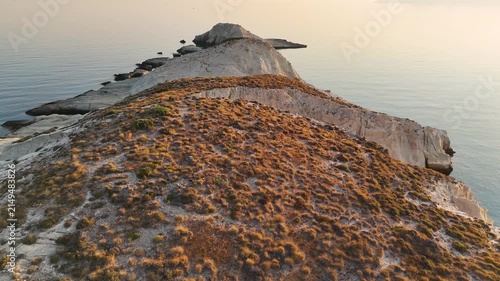 Aerial view captured by drone over the unique rock formations of the Mandrakia region of Milos in Greece. The Aegean sea is calm and quiet with sunrise light reflecting on the surface. 