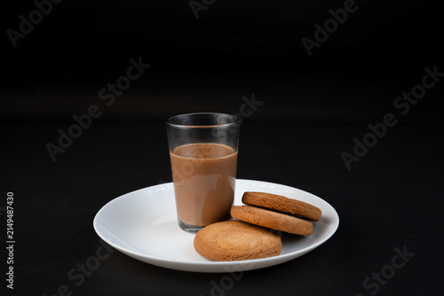 Traditional Indian tea in a clear glass and Biscuit isolated on a black background