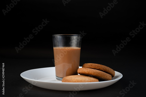Traditional Indian tea in a clear glass and Biscuit isolated on a black background