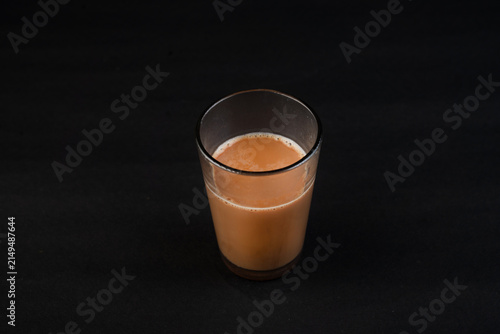Traditional Indian frothy tea in a clear glass isolated on a black background