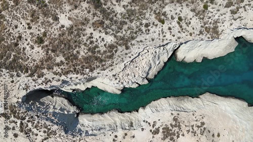 Top down aerial drone view of unique geology found on the island of Milos in Greece. Azure blue ocean water ripples in the sunlight as it makes way through a canyon formed by volcanic rock and ash.