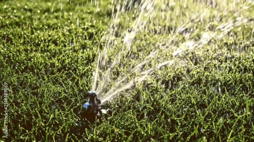 Close up of automatic sprinkler system watering lush green grass lawn on sunny day creating dynamic motion and water droplets footage.