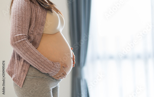 Side view close-up of a pregnant woman holding her belly with both hands.
