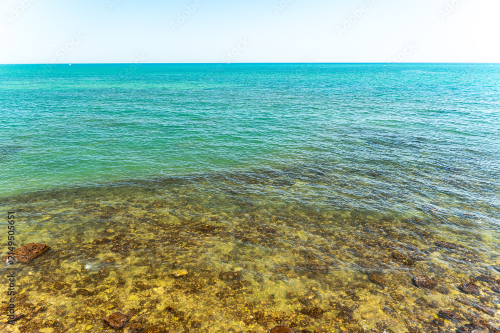 Fototapeta premium Clear turquoise sea water over rocky seabed near shoreline with transparent shallow water revealing underwater stones, concept of summer vacation and nature