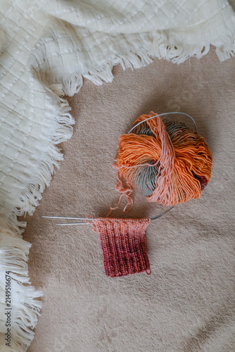 Colourful knitting yarn on knitting needles on cozy sofa. Knitting process. Knitting socks on needles on beige and white plaid. Creative hobbies. Knitting pattern for knitted socks. 