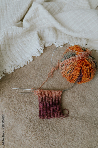 Colourful knitting yarn on knitting needles on cozy sofa. Knitting process. Knitting socks on needles on beige and white plaid. Creative hobbies. Ball of gradient wool