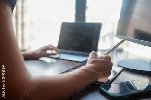 Creative professional focusing on design work from a home office. Skillfully managing multiple digital screens including a tablet with a stylus. A laptop