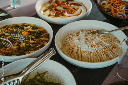 Rich Turkish meze appetizers with hummus, atom yogurt dip, crispy potatoes with garlic herb sauce and fresh vegetable salad on rustic table