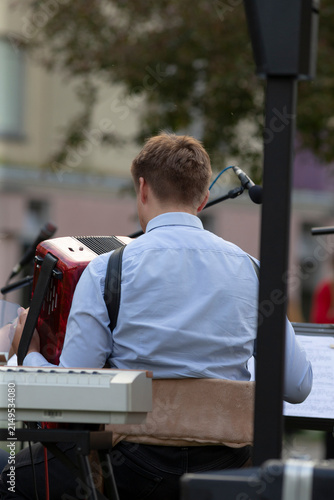 Caucasian teenage accordionist playing red instrument onstage, student soloist vibe with focused hands on buttons, festival audience blurred, youthful