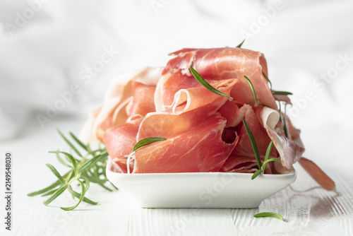 Bild auf Leinwand Prosciutto with rosemary on a white wooden table.