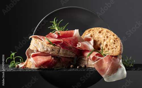 Cuadro en lienzo Ciabatta with prosciutto and rosemary on a black background.