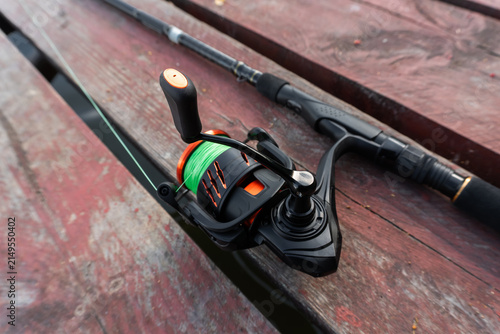 фотографія Spinning fishing rod and reel gear, modern black fishing tackle with neon green line on wooden pier background, angling tackle equipment, predator fish casting rod setup
